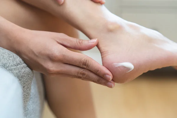 Uśmiechnięta kobieta z cerą pokrytą piegami nakłada krem na twarz.